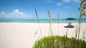 A beach with a green umbrella and a chair, clear blue sky, and ocean. - Golf Membership Available! 2 BR/2BA, Pickleball, Pools, Near Gulf Beaches (Naples)