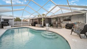 An indoor swimming pool with a glass ceiling, surrounded by lounge chairs and a barbecue area.