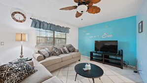 A living room with a sofa, coffee table, TV, and a ceiling fan.
