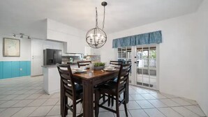 A spacious kitchen with white cabinets, a dining area with a wooden table and chairs, and a large window with blue curtains.