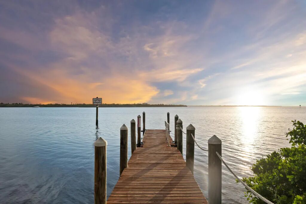 A wooden pier extending into calm water with a sunset in the background.