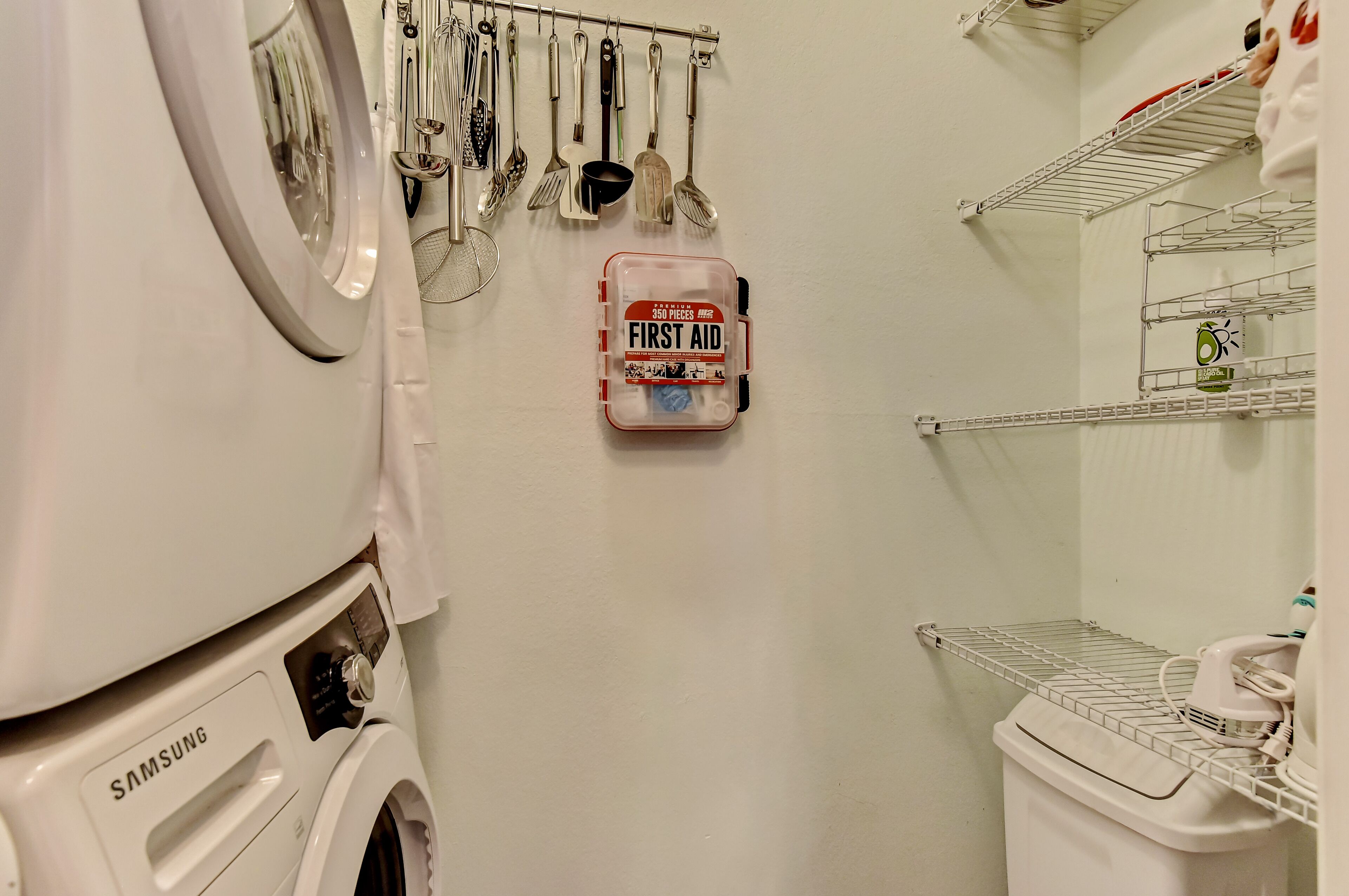 A laundry area with a Samsung washing machine, a first aid kit, and various kitchen utensils hanging on a rack.