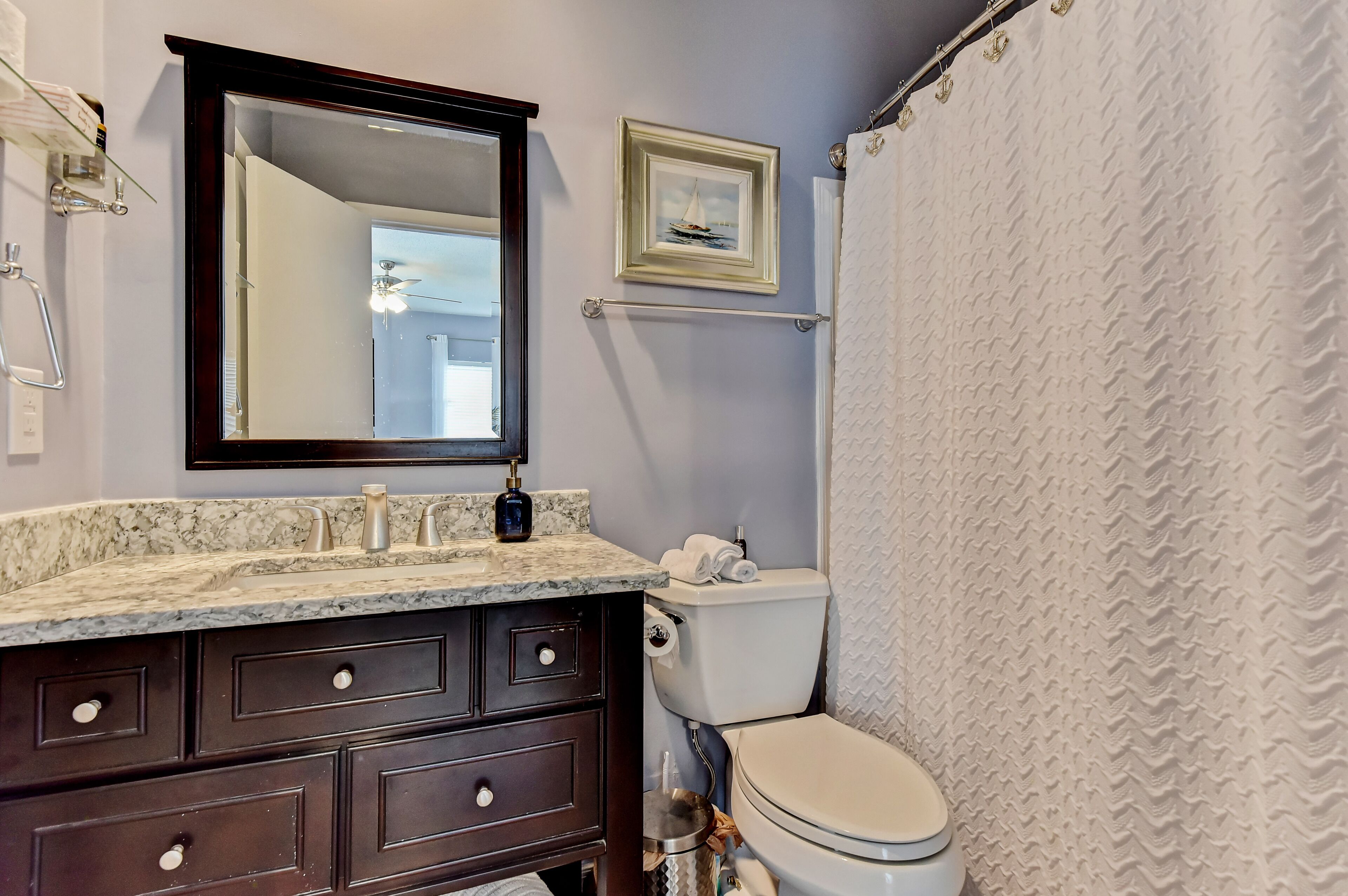 A bathroom with a marble countertop, dark wooden vanity, a framed picture, and a shower curtain.