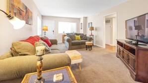 Een woonkamer met een bank, een voetenbankje, een lamp en een televisie.