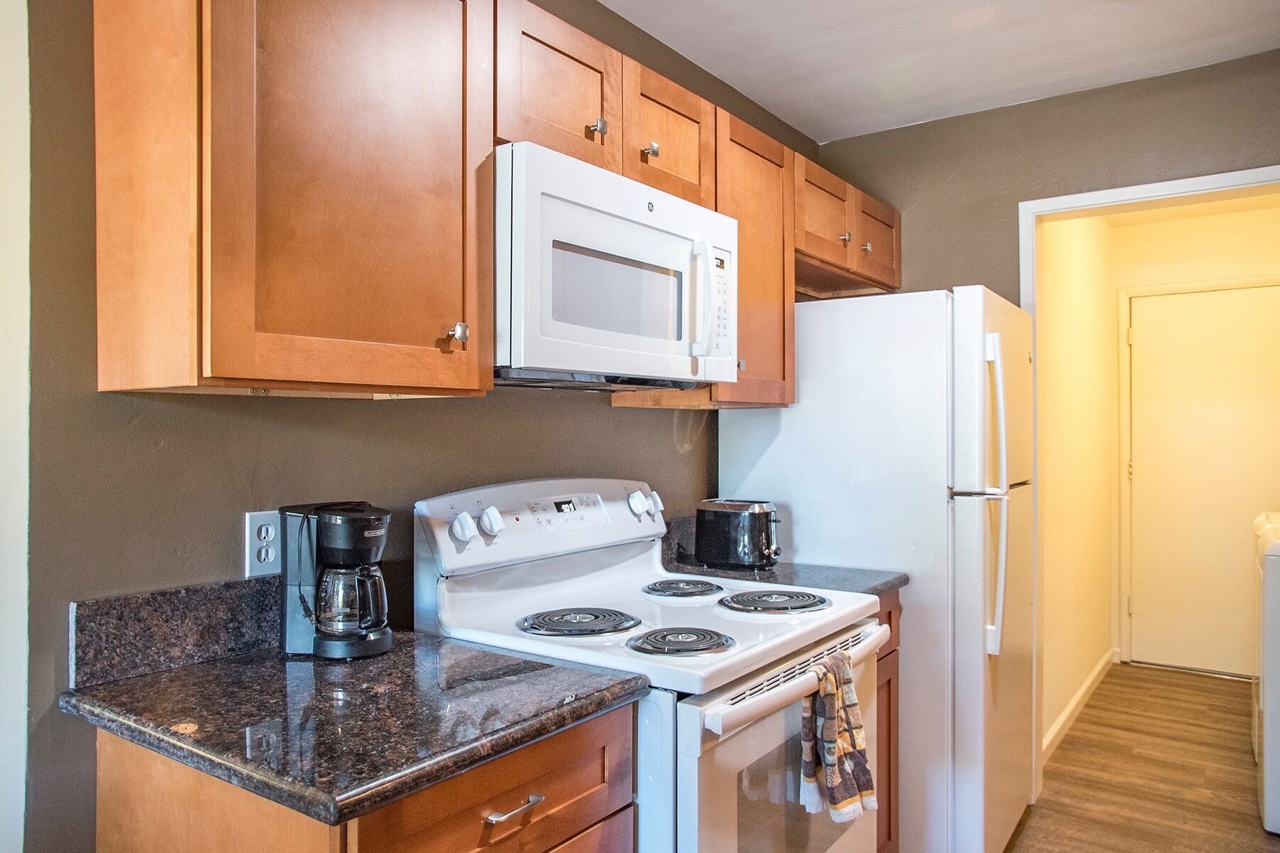 Una cocina con armarios de madera, microondas blanco, refrigerador blanco, estufa y cafetera.