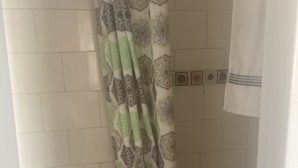 Un baño con inodoro, cortina de ducha estampada con un diseño geométrico y paredes con azulejos.