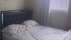 Una cama con cabecera, una ventana con cortinas y un equipo de aire acondicionado en la pared.