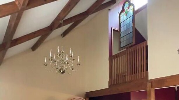 Un salón amplio con techo alto, una araña de cristal, un sofá blanco grande, un televisor y un mueble de madera.