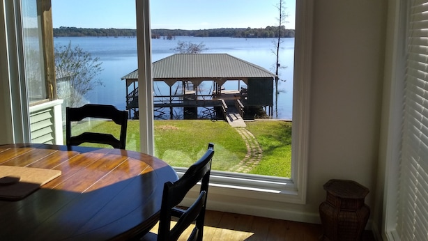 A dining area with a table and chairs, a view of a lake, a dock, and a grassy area. - Parkside Perch on Lake D'Arbonne - Backup Generator and New Boat Cradle (Bernice)
