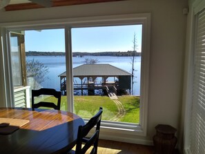 A dining area with a table and chairs, a view of a lake, a dock, and a grassy area. - Parkside Perch on Lake D'Arbonne - Backup Generator and New Boat Cradle (Bernice)