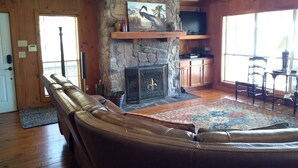 A cozy living room with a stone fireplace, leather sofa, and a television mounted on the wall. - Parkside Perch on Lake D'Arbonne - Backup Generator and New Boat Cradle (Bernice)