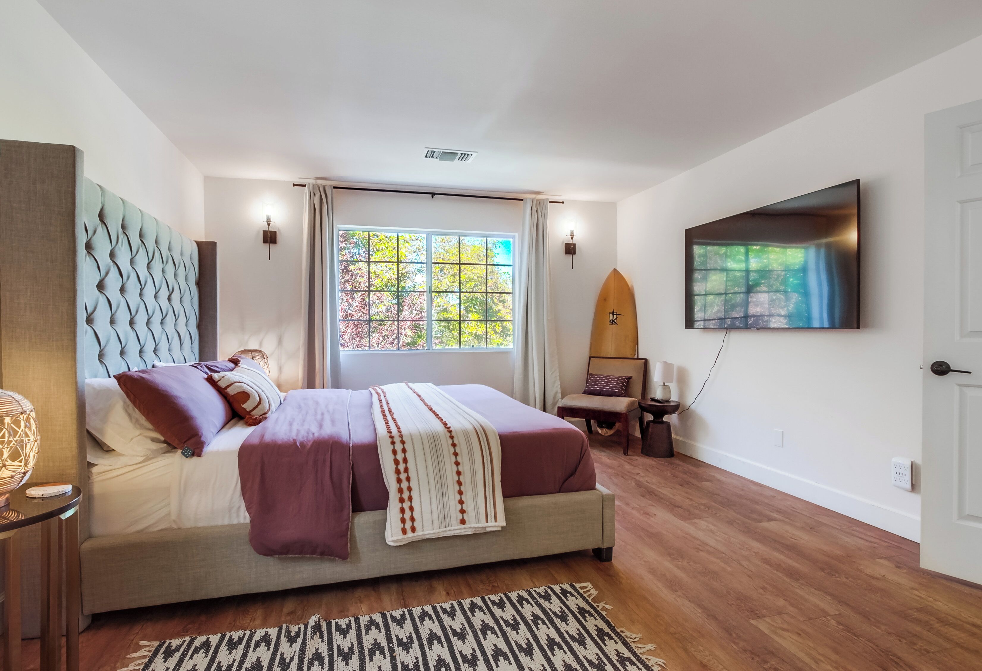 A bedroom with a large bed, a television mounted on the wall, and a window with curtains.