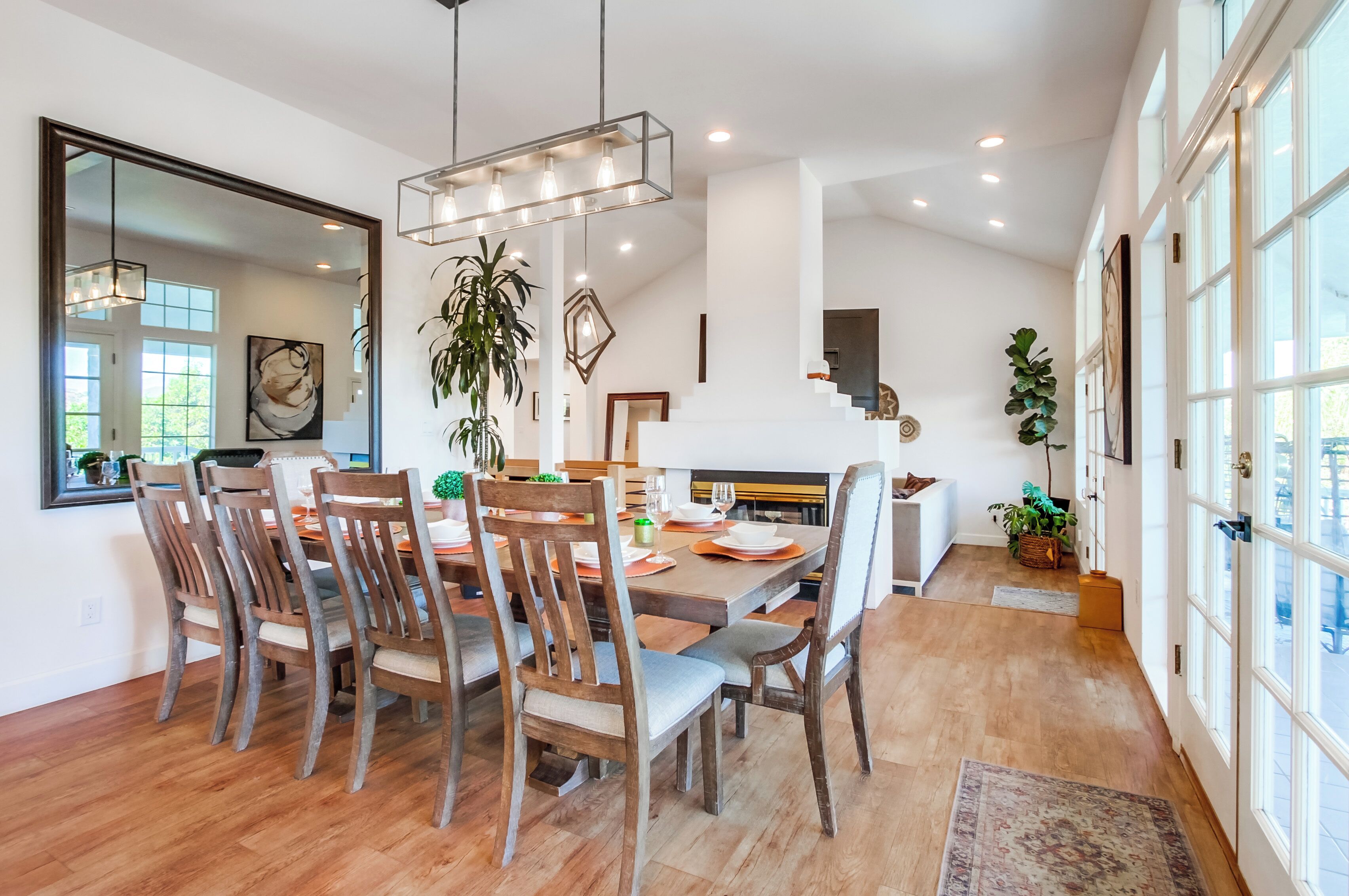 A dining area with a wooden table and chairs, a large mirror, and a hanging light fixture.
