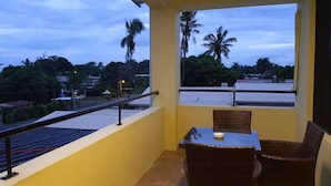 A balcony with a table and chairs, overlooking a residential area with palm trees and houses. - Marigold Apartment 4.  2 bedroom 2nd floor apartment with a great view. (Nadi)