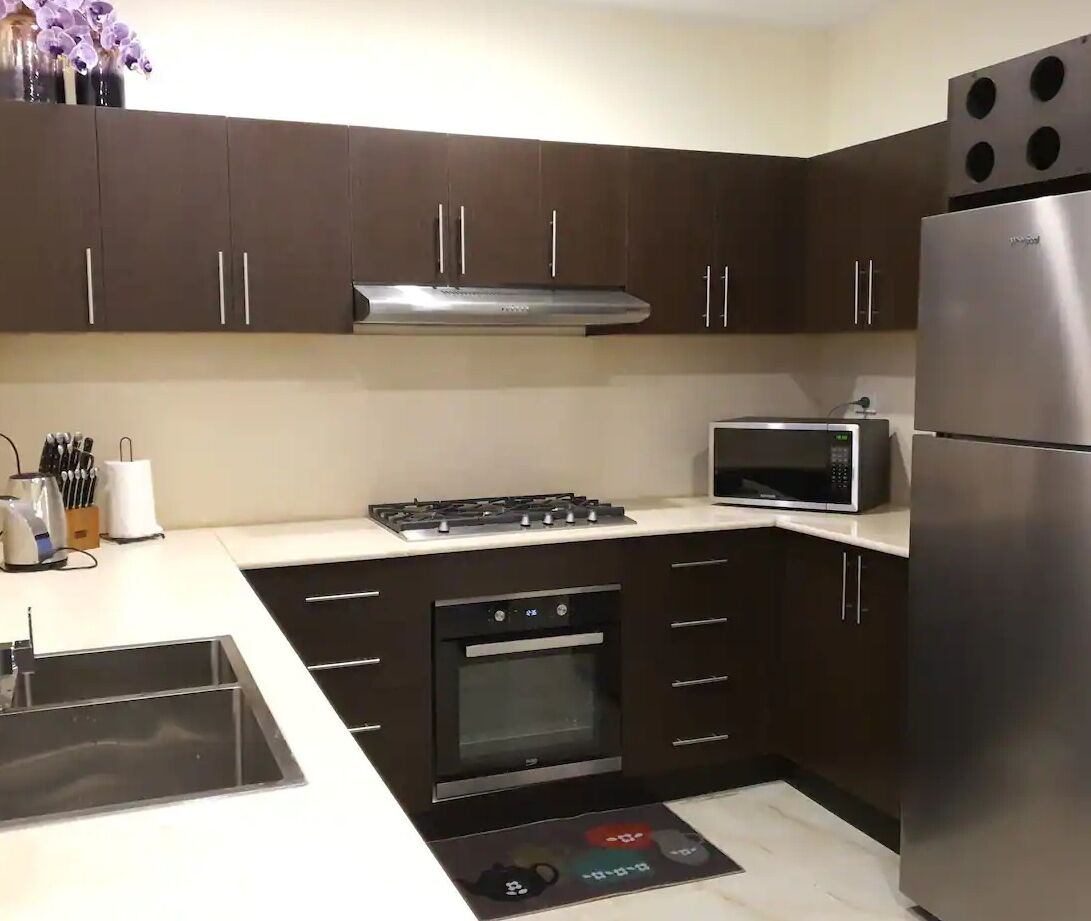 Una cocina moderna con armarios oscuros, estufa de acero inoxidable, microondas y refrigerador.
