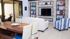 Ein Wohnzimmer mit Sofa, Sesseln, Fernseher und Regalen mit Dekorationsobjekten.