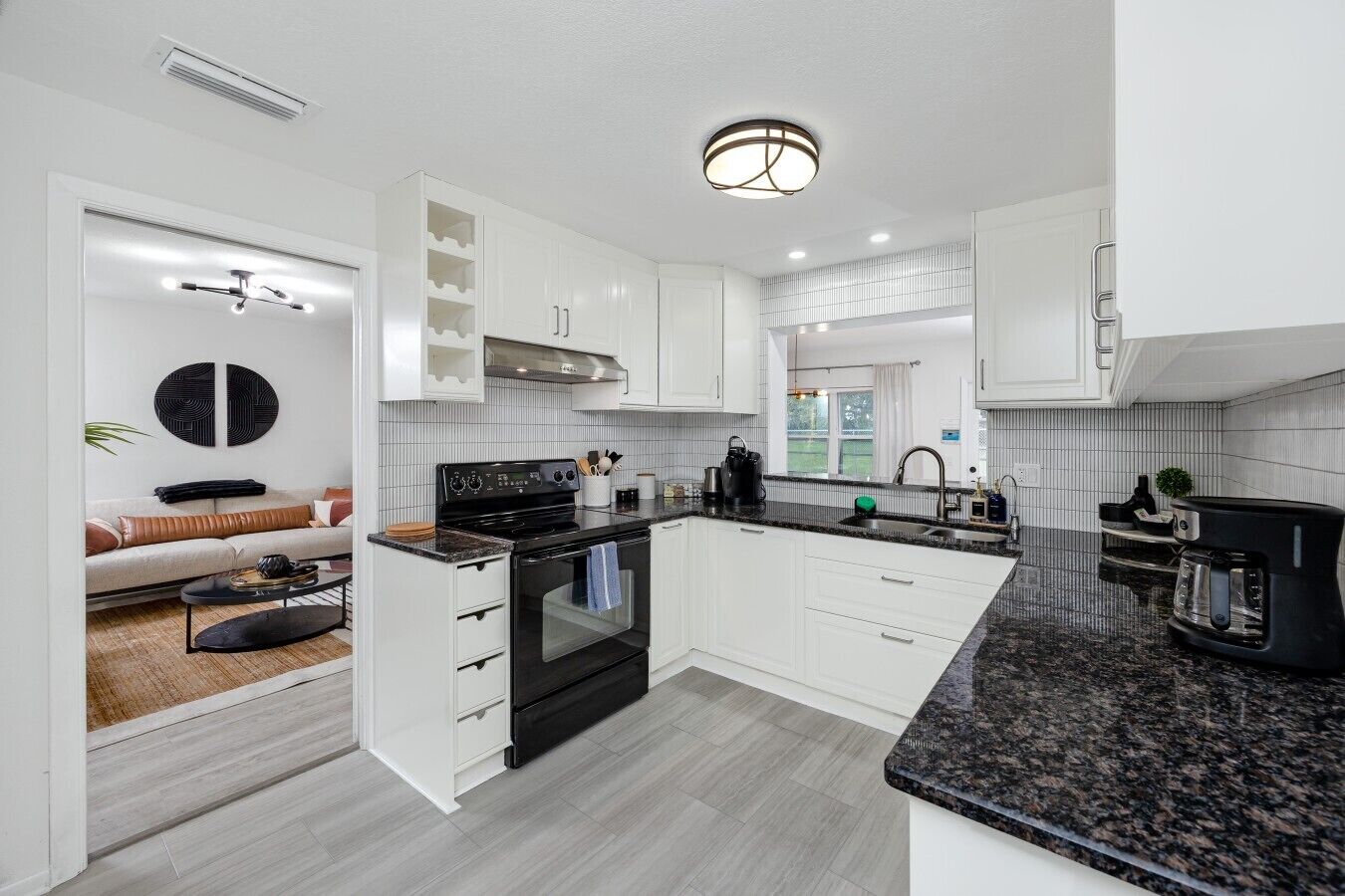 A modern kitchen with white cabinetry, a black stove, and a granite countertop.
