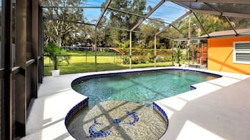 Una piscina con cerramiento de vidrio, rodeada por un jardín y una terraza de madera.