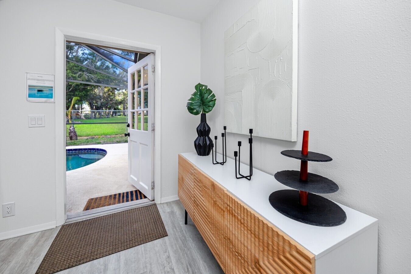 A modern interior with a wooden console, a potted plant, and a pool visible through an open door.