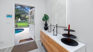 A modern interior with a wooden console, a potted plant, and a pool visible through an open door.