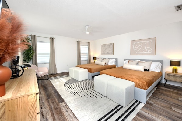 Una habitación de hotel moderna con dos camas, un escritorio de madera, una silla y un ventanal con cortinas.