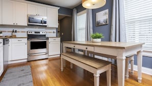 Una cocina con armarios blancos, un microondas, un horno, una mesa de madera y un banco.
