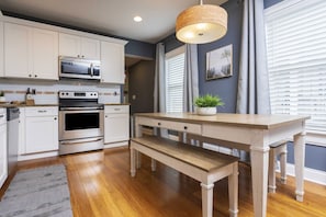 Kitchen features stainless steel appliances, a wooden bench, and a hanging light fixture.