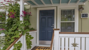 A front porch with a blue door, a white railing, and a 'hello' mat.