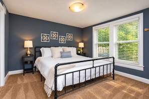 A bedroom with a bed, bedside tables, wall art, a window with blinds, and a ceiling light fixture.