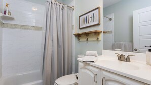 A bathroom with a bathtub, toilet, and sink. There are shelves with toiletries and a framed picture on the wall.