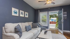 A living room with a beige sofa, patterned cushions, a coffee table, and a ceiling fan.