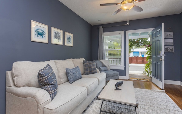 A living room with a beige sofa, patterned cushions, a coffee table, and a ceiling fan.