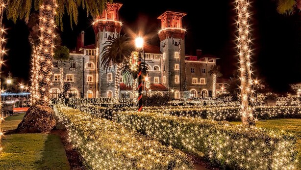 Un edificio histórico con torres iluminadas y un jardín bien cuidado de noche.