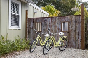 A yellow bicycle parked in front of a wooden fence with a house in the background.
