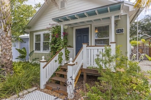 Welcome to a charming home with a front porch and lush greenery, featuring a wooden staircase and white railings.