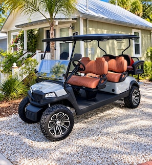 A golf cart parked on a gravel driveway in front of a house with a number sign.