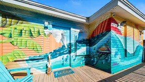 Un edificio colorido con un mural en la pared, una terraza de madera y una alfombra con la palabra 'hello'.