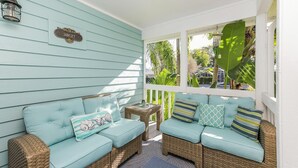 A covered porch with two light blue cushioned sofas and wicker furniture, a small table, and a sign on the wall. - Sunset Beach 2 Bedroom Villa by RedAwning (Holmes Beach)