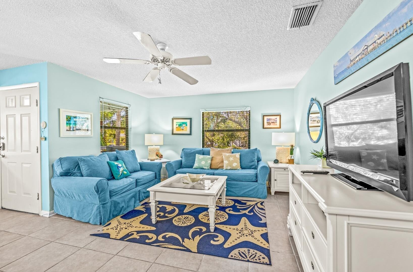 A living room with two blue sofas, a coffee table, a TV, and a ceiling fan.