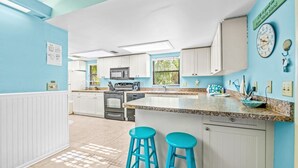 A kitchen with white cabinets, a granite countertop, and blue bar stools. - Sunset Beach 2 Bedroom Villa by RedAwning (Holmes Beach)