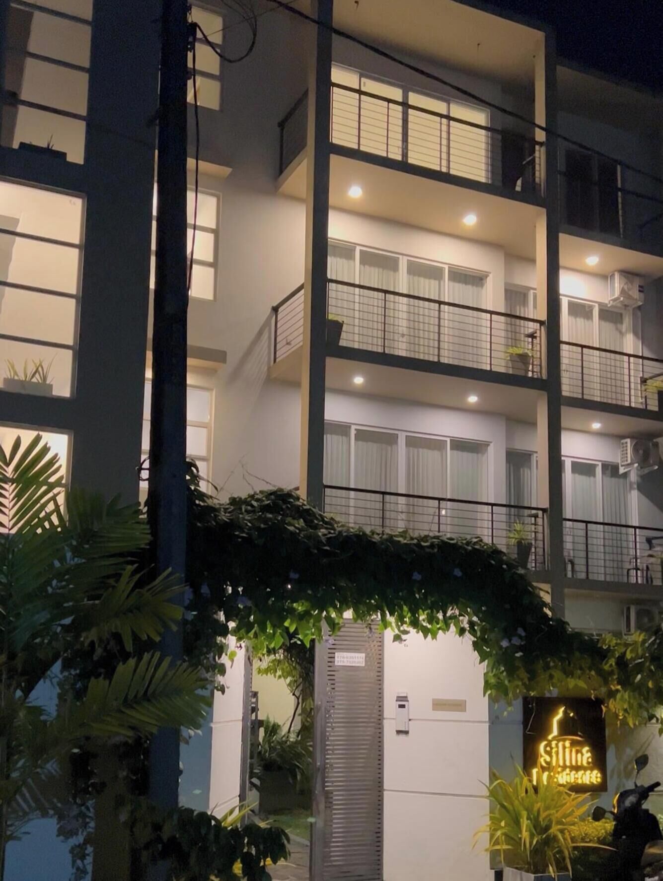 Un immeuble à plusieurs étages doté de balcons, une enseigne indiquant la présence d’un restaurant et une entrée couverte agrémentée de verdure.