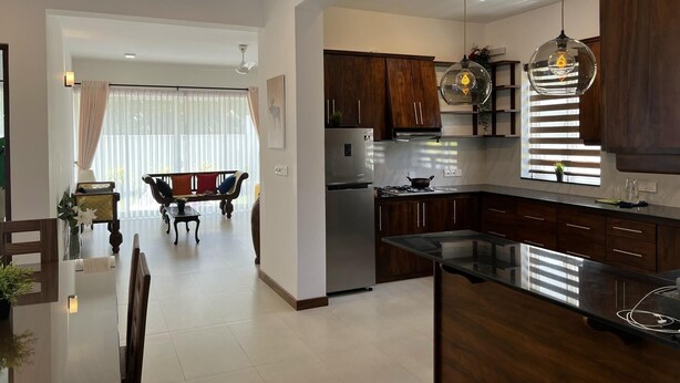 A modern kitchen with dark wooden cabinets, a stainless steel refrigerator, and a black countertop. - Silina Airport Residence in Katunayake (Seeduwa - Katunayake)