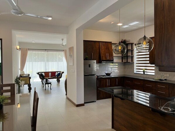 A modern kitchen with dark wooden cabinets, a stainless steel refrigerator, and a black countertop. - Silina Airport Residence in Katunayake (Seeduwa - Katunayake)