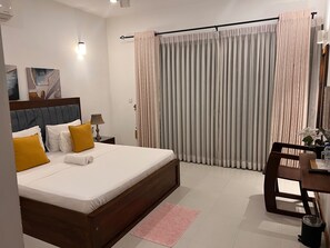 A hotel room with a bed, a desk, a chair, a lamp, and curtains. - Silina Airport Residence in Katunayake (Seeduwa - Katunayake)