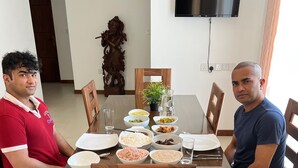 Two people seated at a wooden dining table with various dishes, a potted plant, and a TV mounted on the wall. - Silina Airport Residence in Katunayake (Seeduwa - Katunayake)