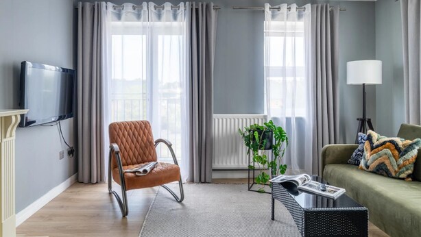 Ein modernes Wohnzimmer mit einem braunen Ledersessel, einem grünen Sofa, einem schwarzen Couchtisch und einer Stehlampe.
