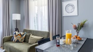 Ein modernes Wohnzimmer mit einer Couch, einem Esstisch mit Frühstücksutensilien und einem großen Fenster mit Vorhängen.