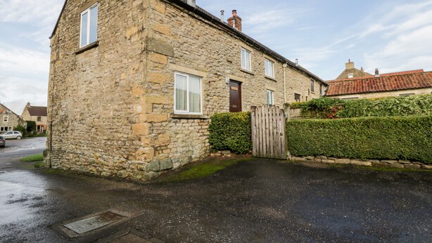 A stone building with a sloped roof, a wooden gate, and a hedge. - Gateside (Pickering)
