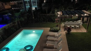 A rectangular swimming pool with a hot tub, lounge chairs, and a covered patio area with tables and chairs.