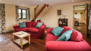A spacious living room with two red sofas, a wooden coffee table, and a staircase leading to another level. - Nine Acres Barn (Marlborough)